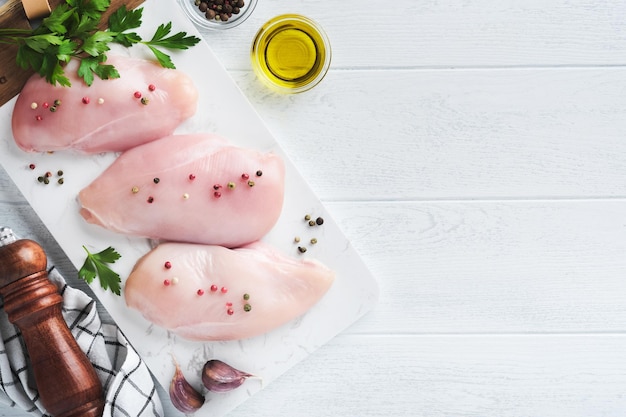 Petto di pollo Due Filetto di pollo con spezie olio d'oliva e prezzemolo su tagliere in pietra bianca su sfondo bianco tavolo in legno Vista dall'alto con spazio di copia Sfondo di cottura di carne di cibo