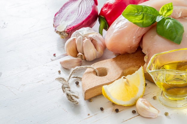 Petto di pollo ed ingredienti su fondo di legno bianco