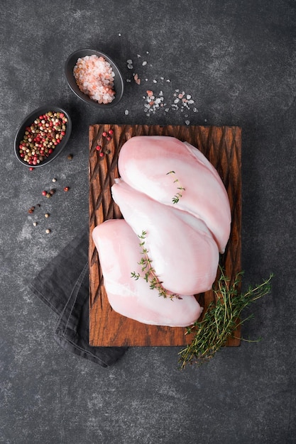 Petto di pollo Filetti di petto di pollo crudo su tagliere di legno con erbe e spezie su sfondo nero Vista dall'alto con spazio per la copia