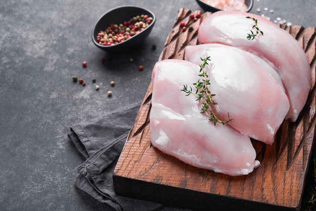 Petto di pollo Filetti di petto di pollo crudo su tagliere di legno con erbe e spezie su sfondo nero Vista dall'alto con spazio per la copia