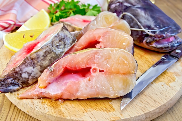 Pezzi affettati crudi di pesce gatto su una tavola circolare, prezzemolo, limone, tovagliolo, coltello su uno sfondo di tavole di legno