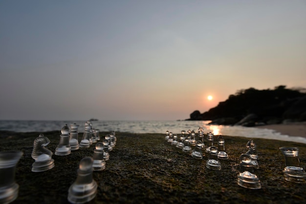 Pezzi degli scacchi su una scacchiera naturale (roccia) con il mare al tramonto sullo sfondo