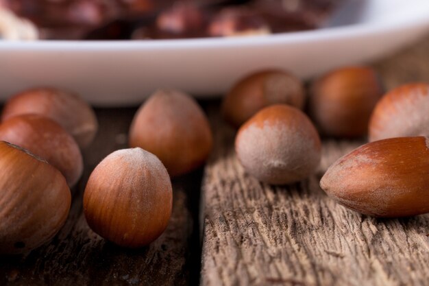 Pezzi del cioccolato con le nocciole sul fondo di legno del piatto bianco. avvicinamento.