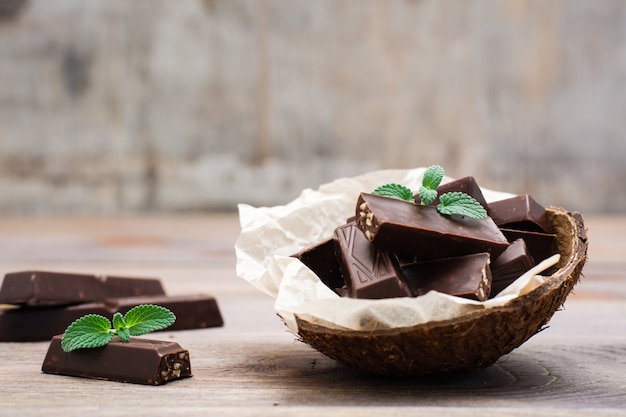 Pezzi del cioccolato e foglie di menta in una ciotola e su una tavola di legno. Il concetto di sovrappeso dai dolci. Stile rustico