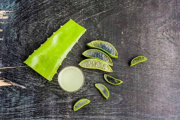 Pezzi di aloe vera e gel di aloe nel bicchiere su un vecchio sfondo di legno scuro