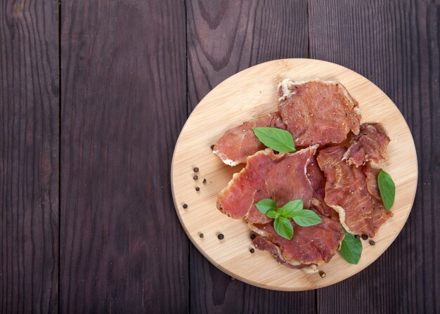 Pezzi di carne a scatti con foglie di basilico giacciono su un tagliere di legno su uno sfondo di legno.