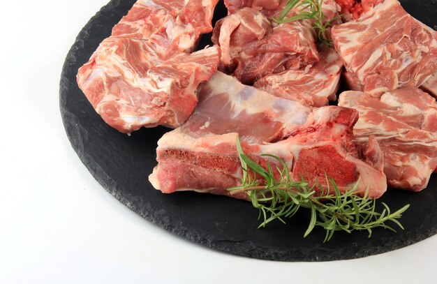 Pezzi di carne cruda su una lastra di pietra nera rotonda su fondo bianco, Carne fresca con ossa