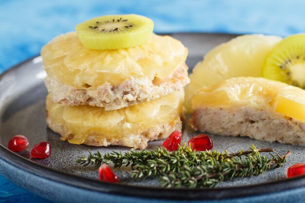 Pezzi di carne di maiale al forno con formaggio di ananas e kiwi sul piatto grigio e sfondo blu