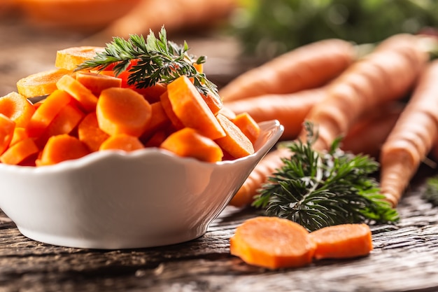 Pezzi di carota affettati in una ciotola e un mazzetto di carote fresche sullo sfondo.