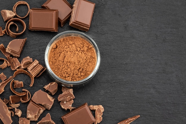 Pezzi di cioccolato rotti e cacao in polvere su una superficie scura. Vista dall'alto con copyspace per il testo.