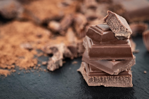 Pezzi di cioccolato rotti e polvere di cacao su uno sfondo scuro.