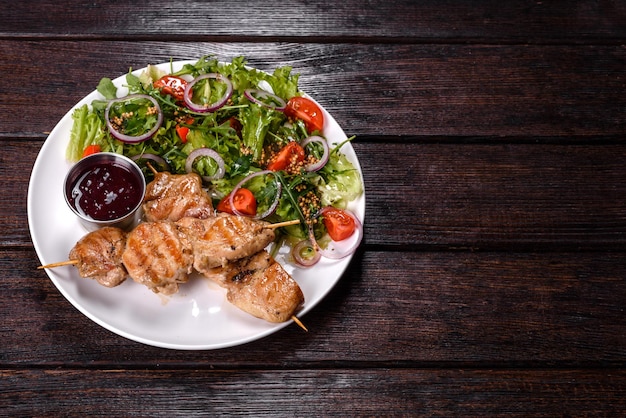 Pezzi di filetto di pollo al forno su bastoncini di legno grigliati con insalata e salsa rossa. Preparazione della tavola festiva