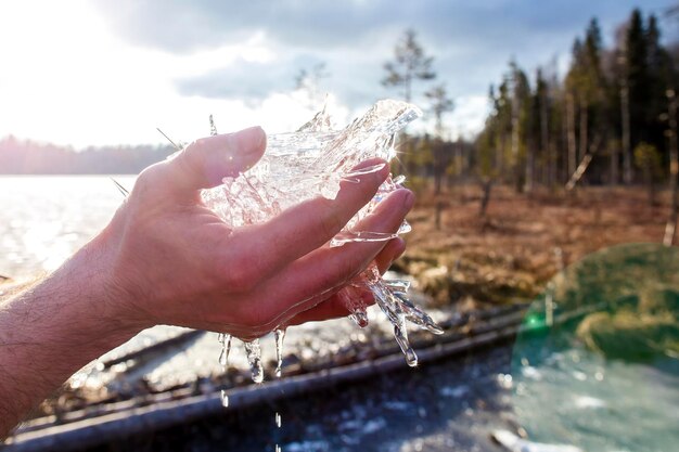 Pezzi di ghiaccio in fusione rotto tenuti in mano vicino al fiume che scorre nel lago vicino alla foresta