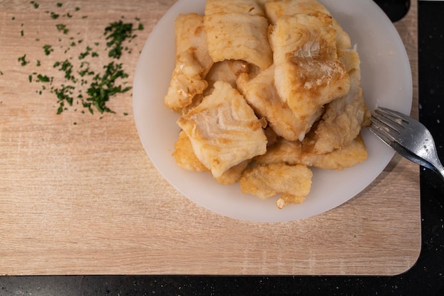 Pezzi di lombi di nasello fritti su piatto bianco tagliere di legno Preparazione della ricetta spagnola del nasello romano