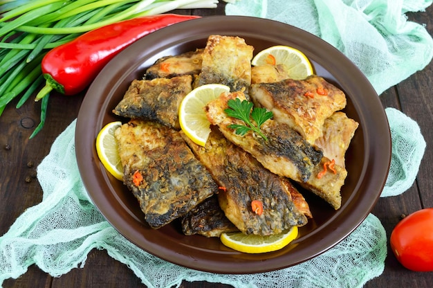 Pezzi di pesce fritto (carpa) su un piatto di ceramica su uno sfondo di legno scuro.