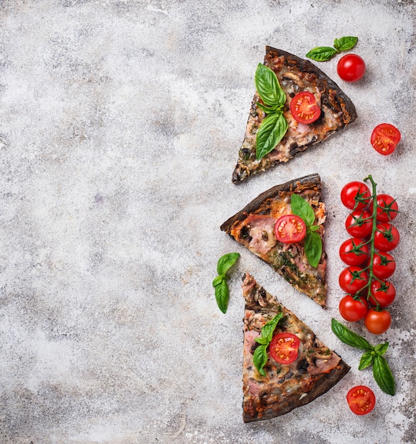 Pezzi di pizza nera con pomodori e basilico