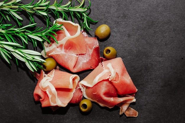 Pezzi di prosciutto di maiale essiccato con olive su una tavola nera