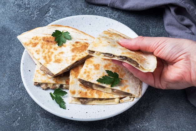 Pezzi di quesadilla con funghi panna acida e formaggio su un piatto con foglie di prezzemolo.