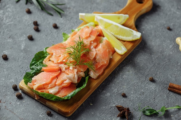 Pezzi di salmone fritto con aneto e spicchi di limone su una tavola di legno.