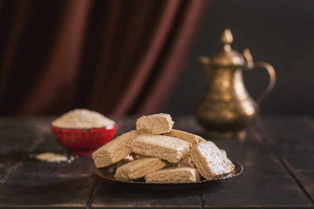 Pezzi di tahini halva, semi di sesamo in una ciotola, una brocca vintage