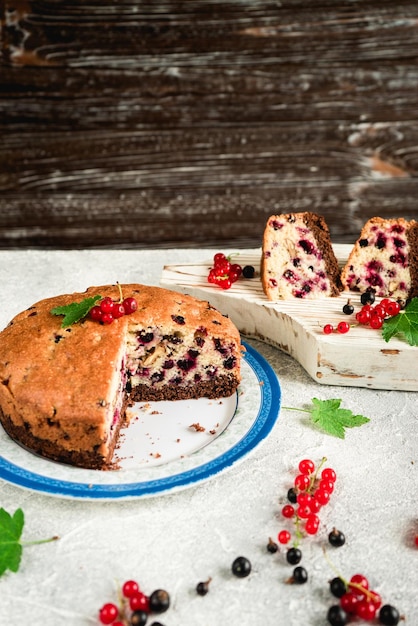 Pezzi di torta di frutti di bosco a fette con ribes nero e rosso su sfondo grigio cemento 1