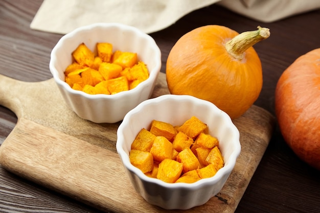 Pezzi di zucca al forno in ciotole di ceramica bianca sul tagliere sulla tavola di legno marrone