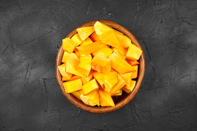 Pezzi di zucca in una ciotola di legno rotonda sulla tavola nera, vista dall'alto. Zucca tritata (zucca) in un piatto di insalata. Cucinare cibo vegetale