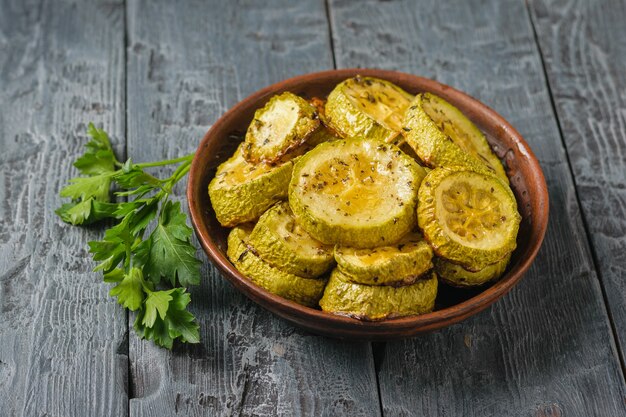 Pezzi di zucchine al forno in una ciotola di argilla con erbe su un tavolo di legno