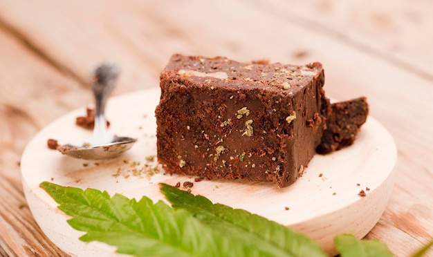 pezzo di brownie con marijuana su tavola di legno con cucchiaio e foglia di cannabis verde