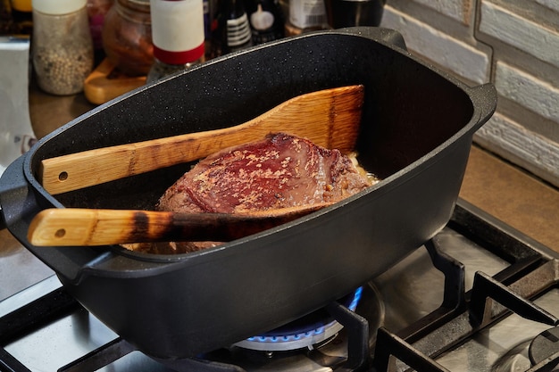 Pezzo di carne è fritto con cipolle in salsa di vino in padella rettangolare sul fuoco su fornello a gas Spatole di legno