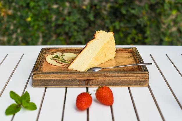 Pezzo di cheesecake su una tavola di legno con fragola e menta su tavolo di legno bianco con foglia verde