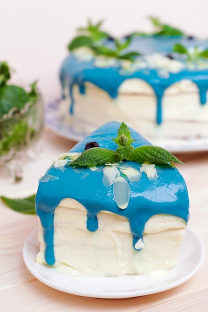 Pezzo di dolce decorato con crema blu, menta e mirtilli su un tavolo di legno.