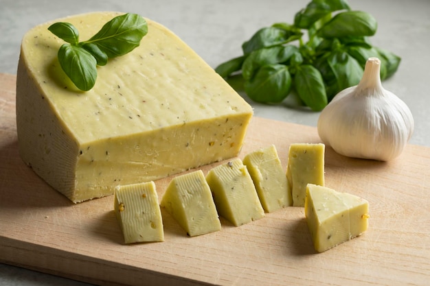 Pezzo di formaggio biologico olandese con foglie di aglio e basilico