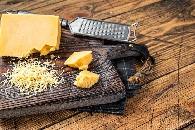 Pezzo di formaggio cheddar grattugiato su una tavola di legno. Fondo in legno. Vista dall'alto. Copia spazio.