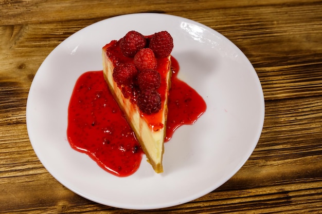 Pezzo di gustosa cheesecake di New York con lamponi e marmellata di lamponi in un piatto bianco sul tavolo di legno