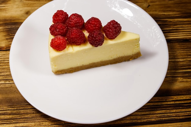 Pezzo di gustosa cheesecake di New York con lamponi in un piatto bianco su un tavolo di legno