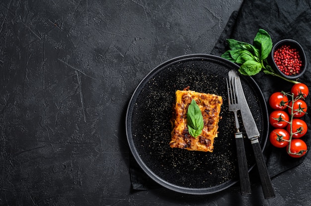 Pezzo di gustosa lasagna calda. Cibo italiano tradizionale. Muro nero. Vista dall'alto. Spazio per il testo