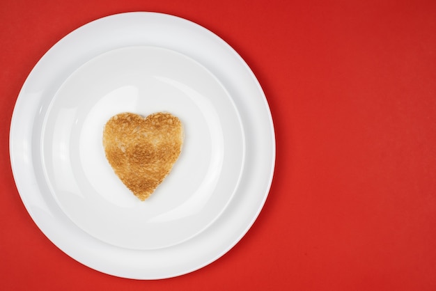 Pezzo di pane tagliato a forma di cuore isolato sul piatto bianco