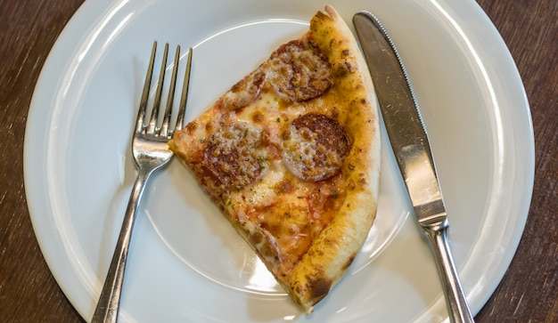 Pezzo di pizza calda fresca con salsiccia ai peperoni e mozzarella cosparsa di erbe. Messa a fuoco selettiva, vista dall'alto