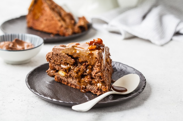 Pezzo di snickers fatti in casa torta con crema di cioccolato e caramello su un piattino nero, sfondo bianco.