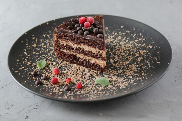 Pezzo di torta al cioccolato su un piatto nero decorato con bacche rosse e foglie di menta.