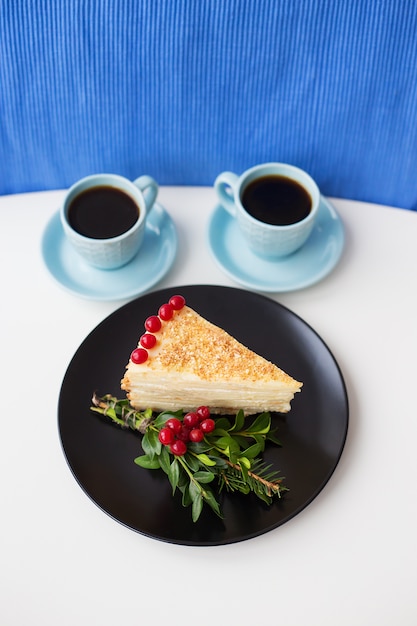 Pezzo di torta decorata con rami e bacche e tazze di caffè