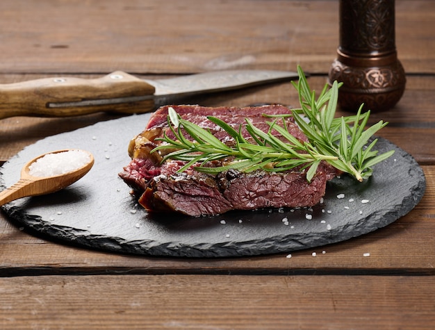 Pezzo fritto di ribeye di manzo tagliato a pezzi su un tagliere nero, raro grado di cottura. Bistecca deliziosa