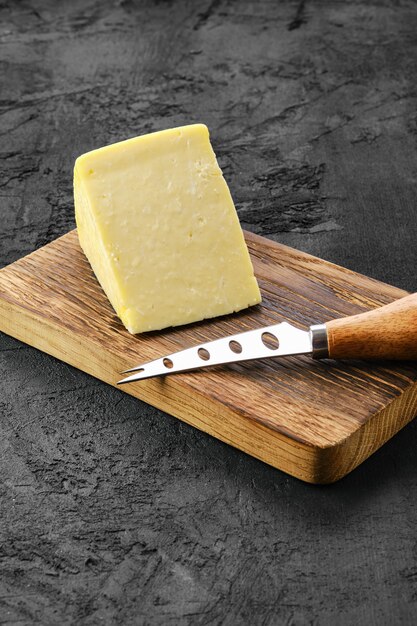 Pezzo triangolare di formaggio a pasta dura sul tagliere di legno