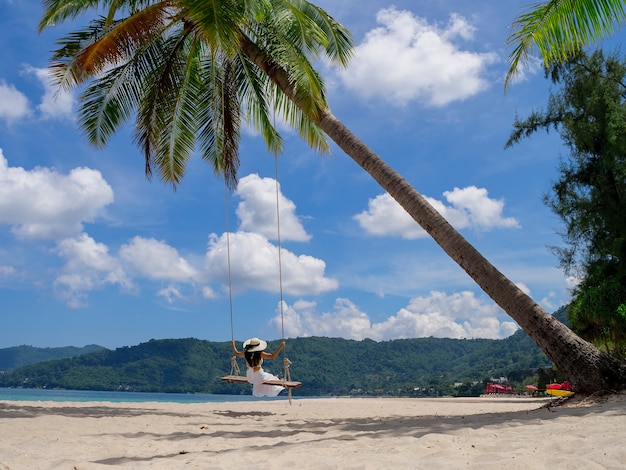 Phuket Thailandia Paradiso della spiaggia tropicale con altalena da spiaggia con ragazza in camicia bianca Le donne si rilassano sull'altalena sotto la palma da cocco in una bellissima spiaggia tropicale di sabbia bianca