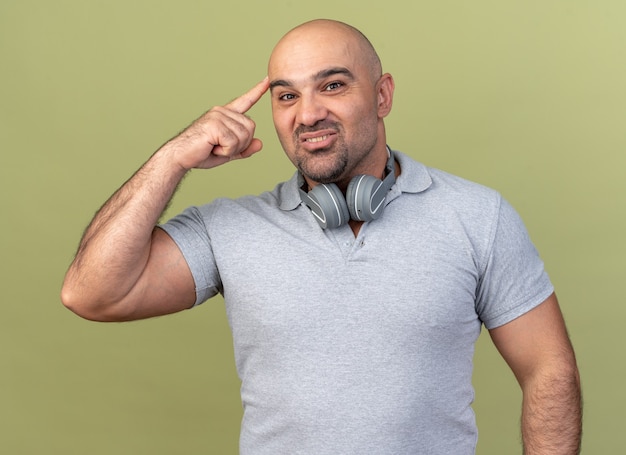 Piacere casual uomo di mezza età che indossa le cuffie sul collo guardando davanti facendo pensare gesto isolato sulla parete verde oliva