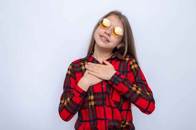 Piacere di mettere le mani sul cuore bella bambina che indossa camicia rossa e occhiali isolati sul muro bianco