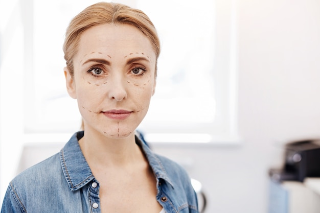 Piacevole bella donna bionda in piedi e ti guarda mentre ha segni sul viso