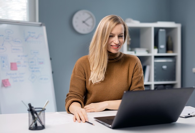 Piacevole donna caucasica con i capelli biondi seduta alla scrivania dell'ufficio e al lavoro su un laptop moderno Donna d'affari che analizza la situazione aziendale sul posto di lavoro