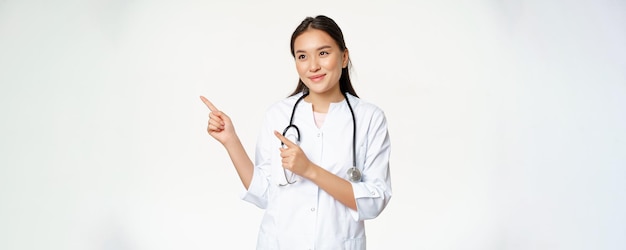 Piacevole dottoressa sorridente in uniforme che punta le dita e guarda a sinistra con uno smi amichevole premuroso